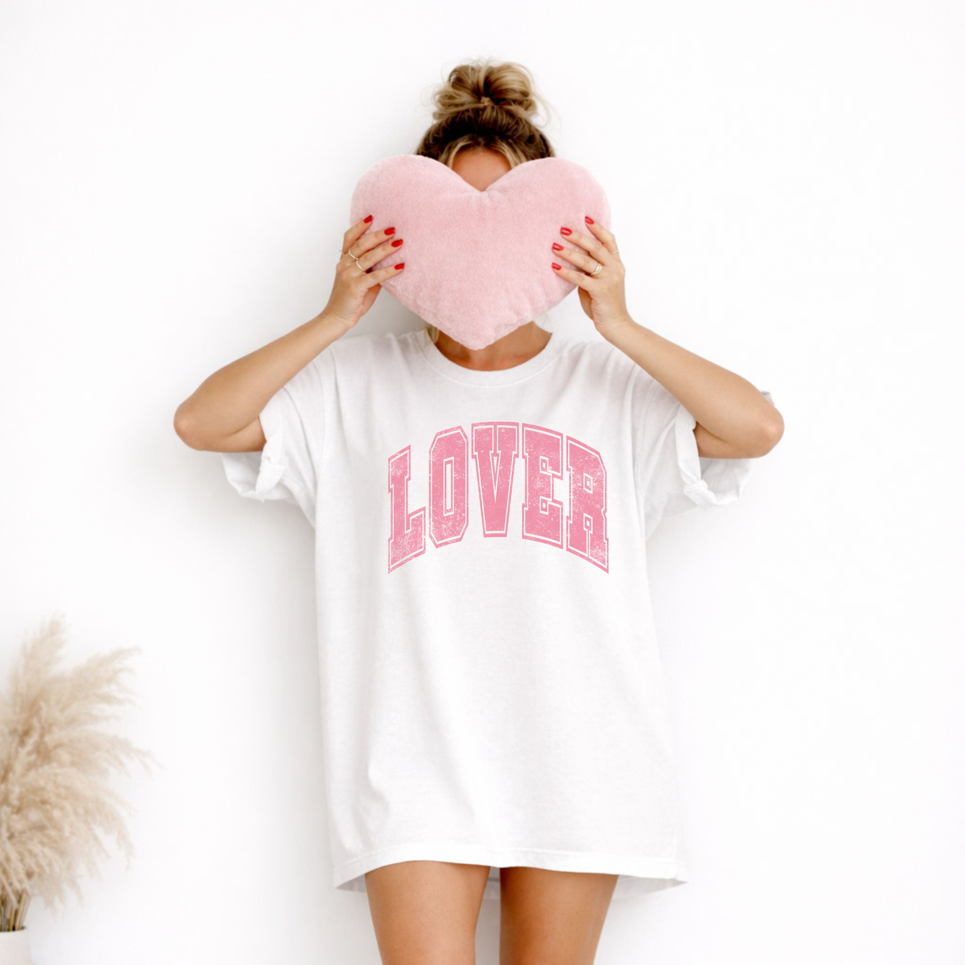 Model wearing white Lover graphic tee holding pink heart pillow, oversized relaxed fit