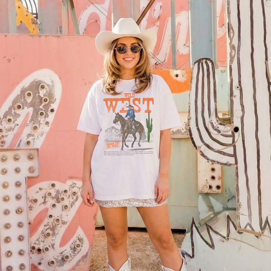 Model wearing Wild West graphic tee styled with cowboy boots and western backdrop