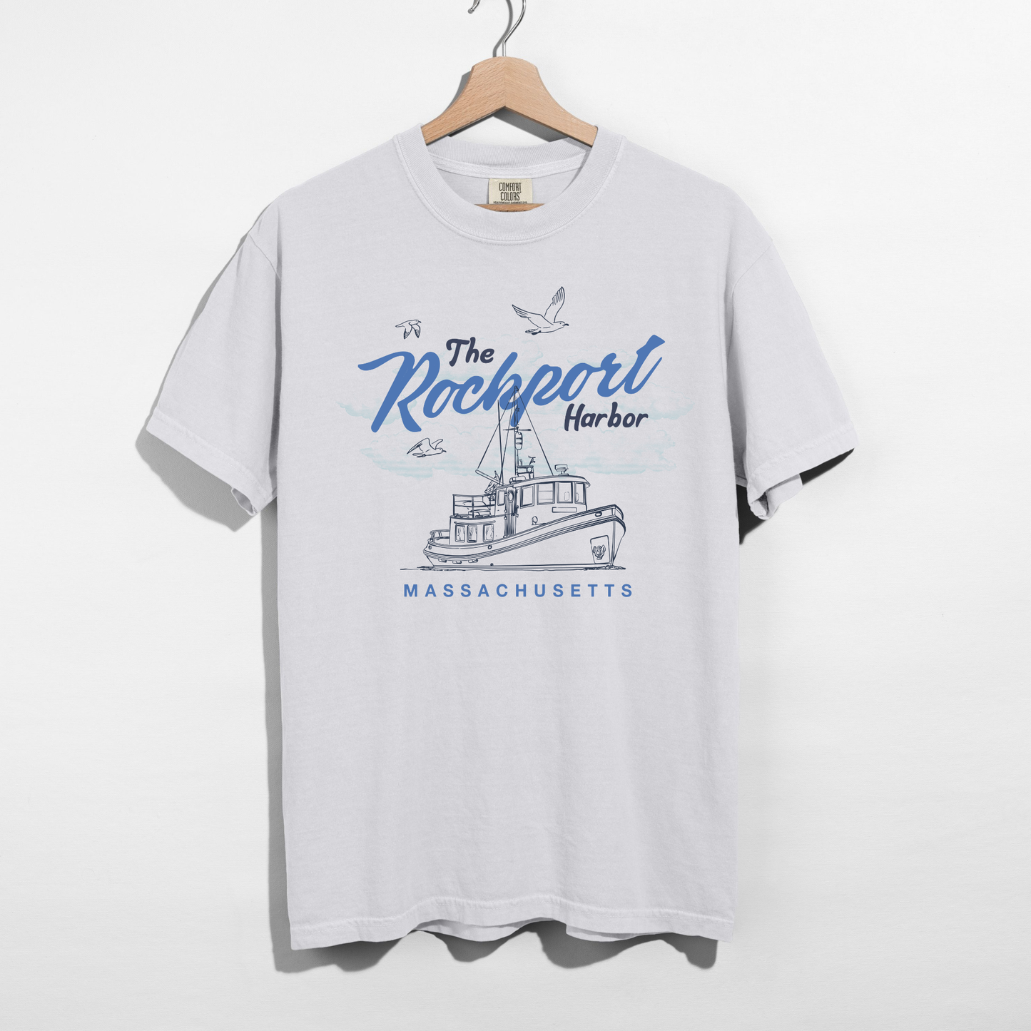 White t-shirt with 'The Rockport Harbor, Massachusetts' graphic on a hanger against a white background