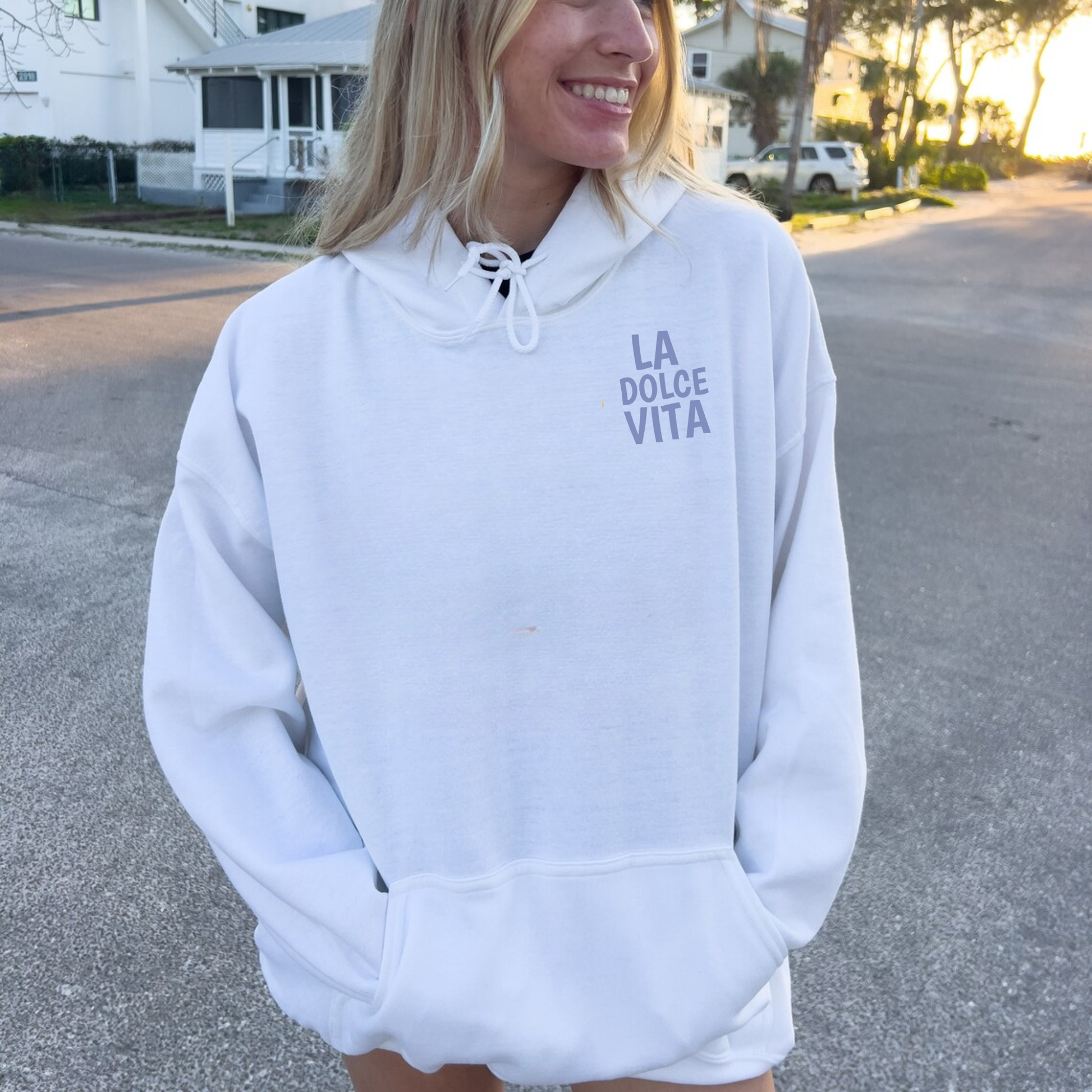 Model wearing white La Dolce Vita coastal hoodie with minimalist front text outdoors