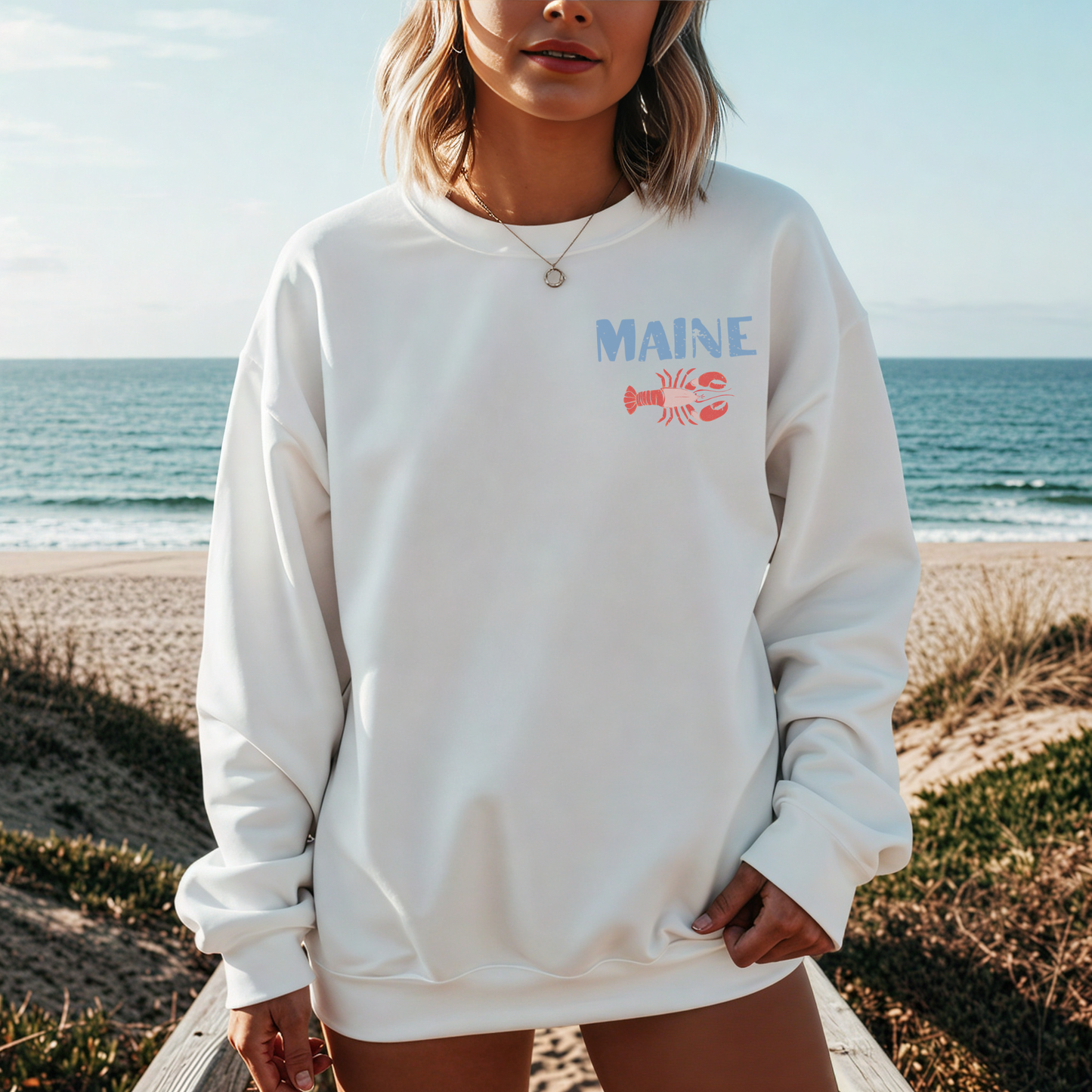 Woman wearing white Maine lobster seafood club crewneck sweatshirt at the beach with ocean background
