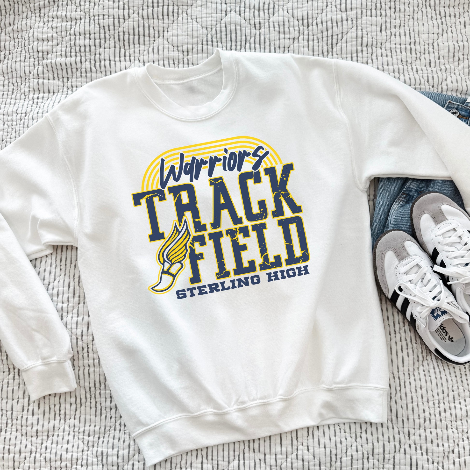 White Sterling High Warriors Track and Field crewneck sweatshirt styled flat on a bed with sneakers, featuring school spirit graphic.