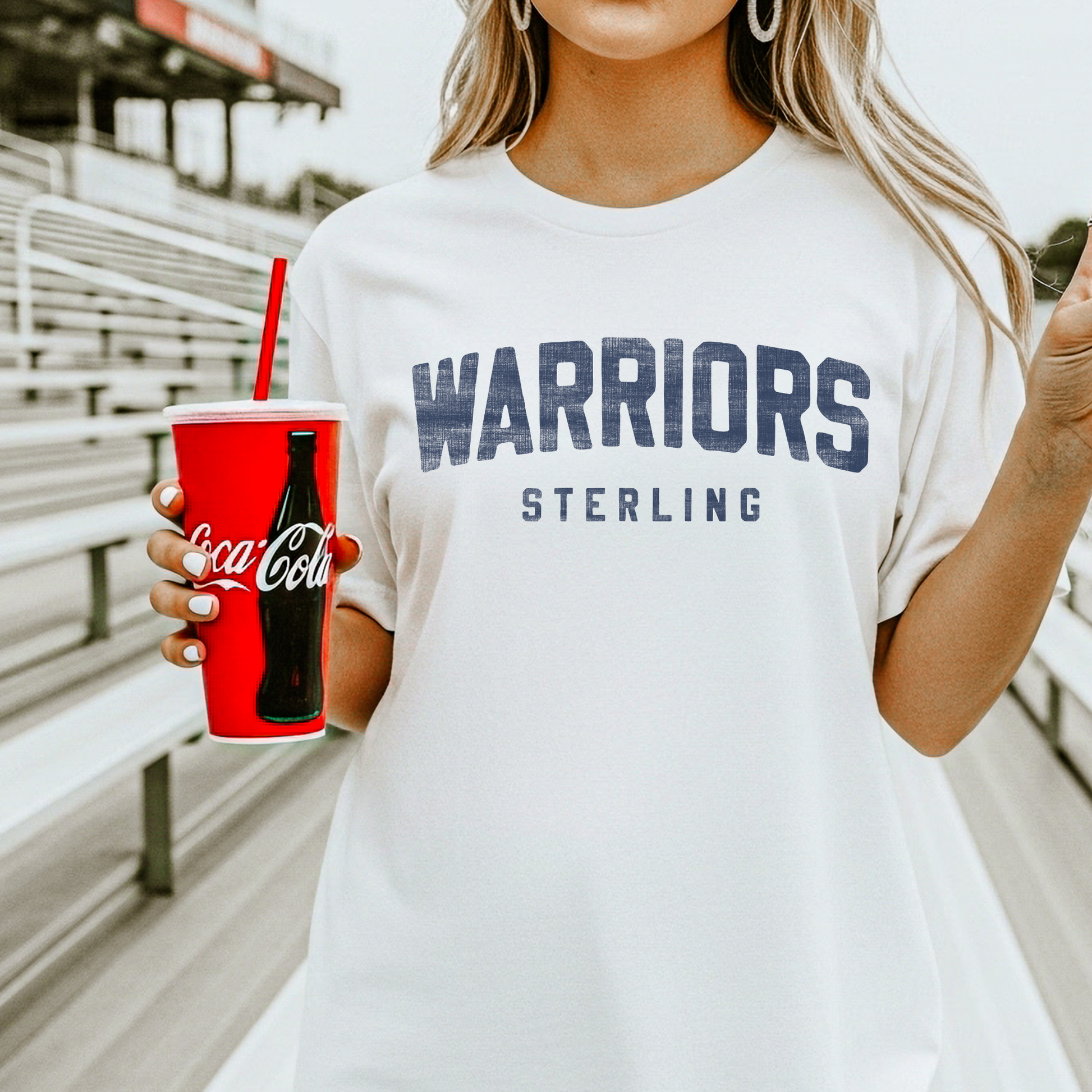 Sterling Warriors graphic t-shirt worn by model at stadium bleachers showing vintage school spirit design