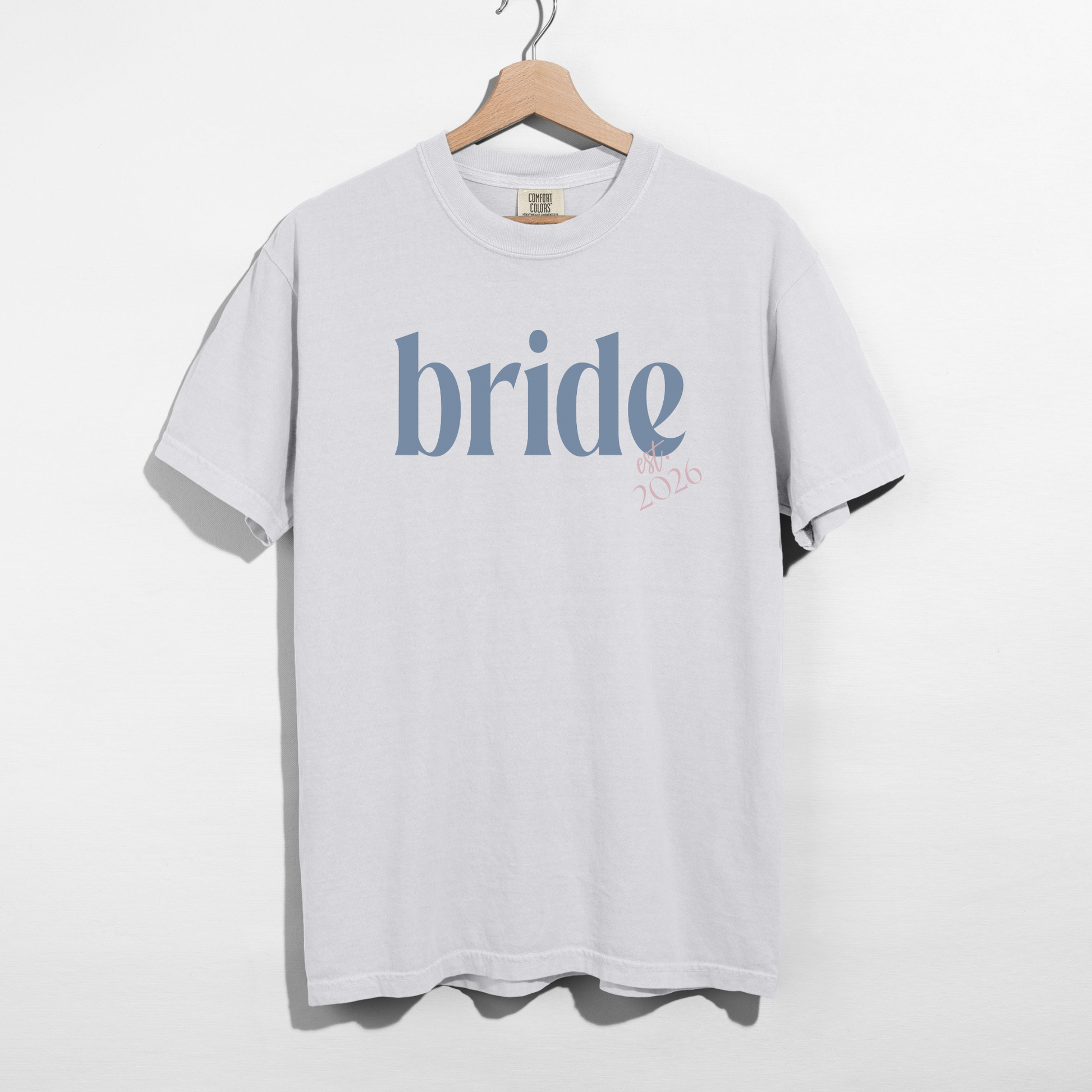 White t-shirt with 'bride' printed on it, hanging on a wooden hanger against a white background.