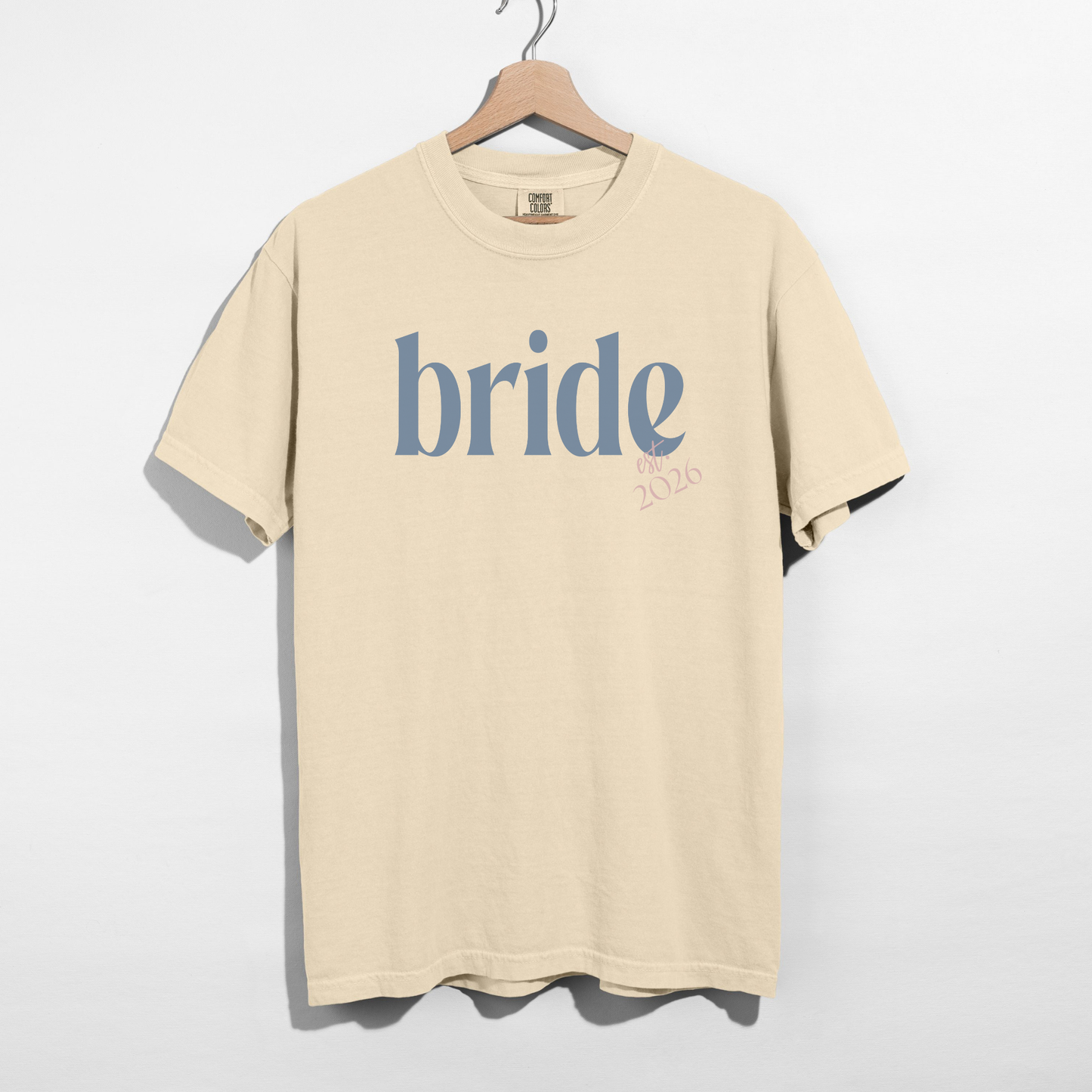 Beige t-shirt with 'bride' printed on it, hanging on a wooden hanger against a white background.