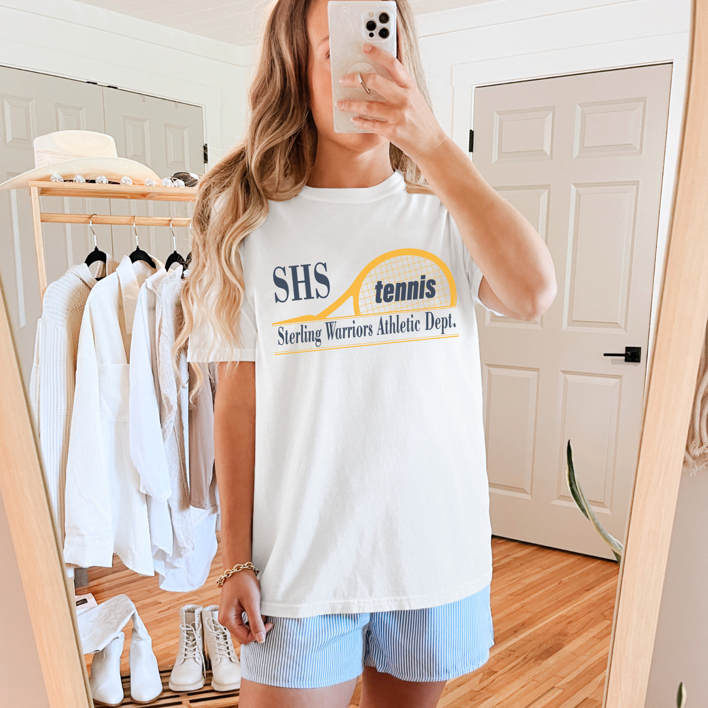 Woman wearing an white SHS Tennis Sterling Warriors Athletic Dept. t-shirt styled casually with shorts