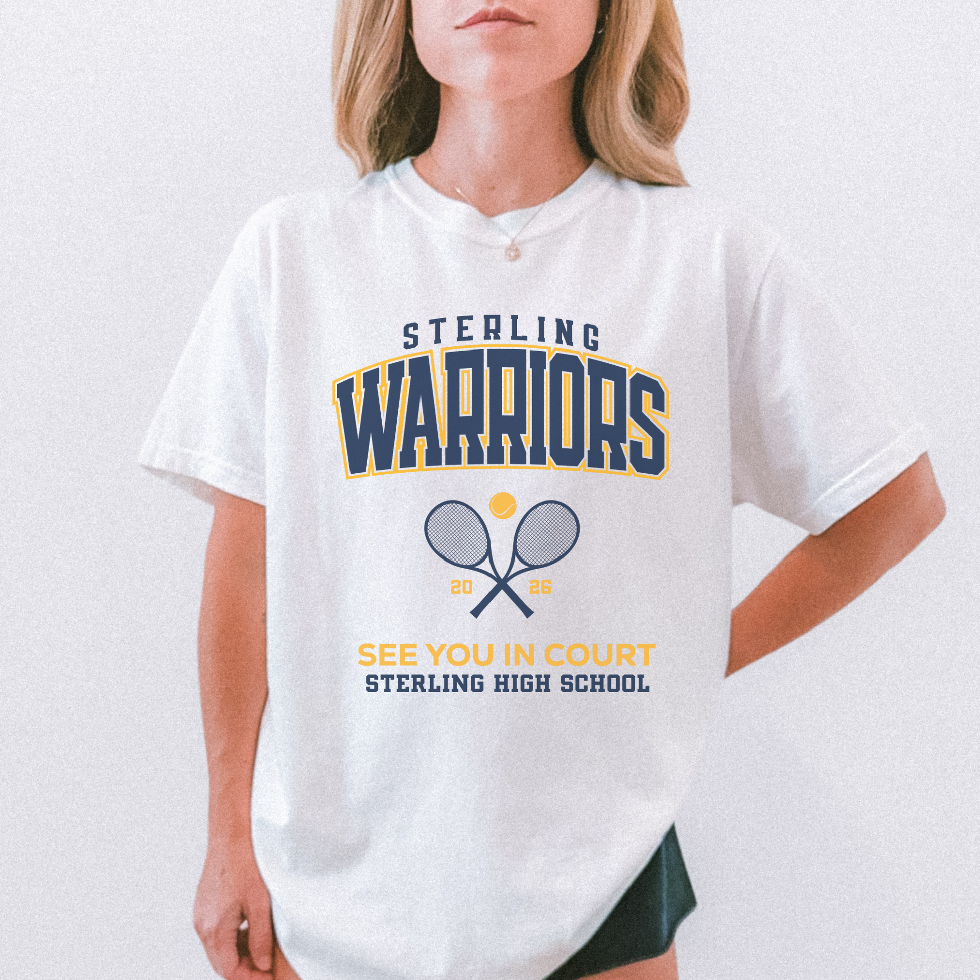 Woman wearing a white Sterling Warriors Tennis t-shirt featuring crossed tennis rackets and collegiate design