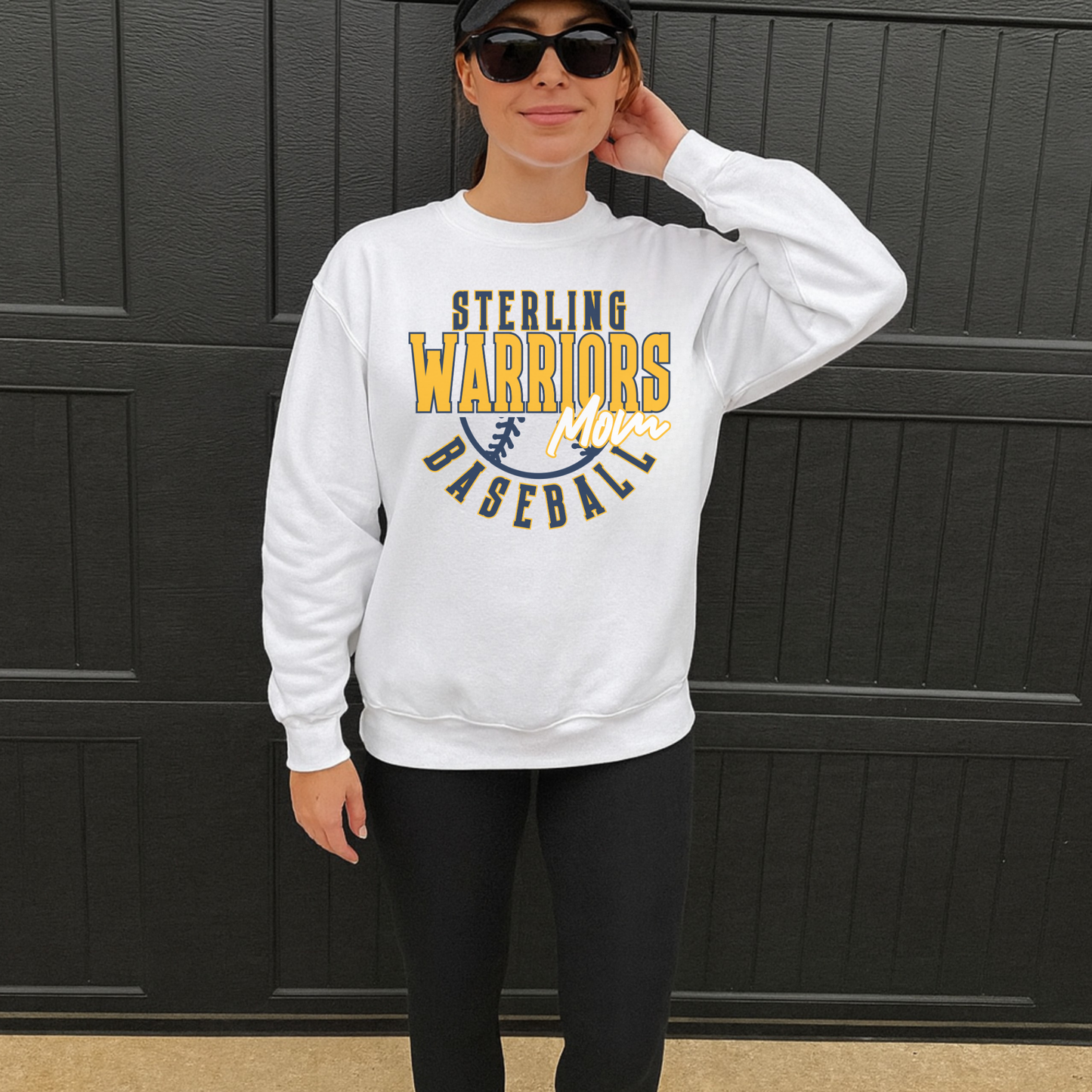 Sterling Warriors Baseball Mom white crewneck sweatshirt worn by woman with black leggings and hat standing outdoors sporty casual outfit