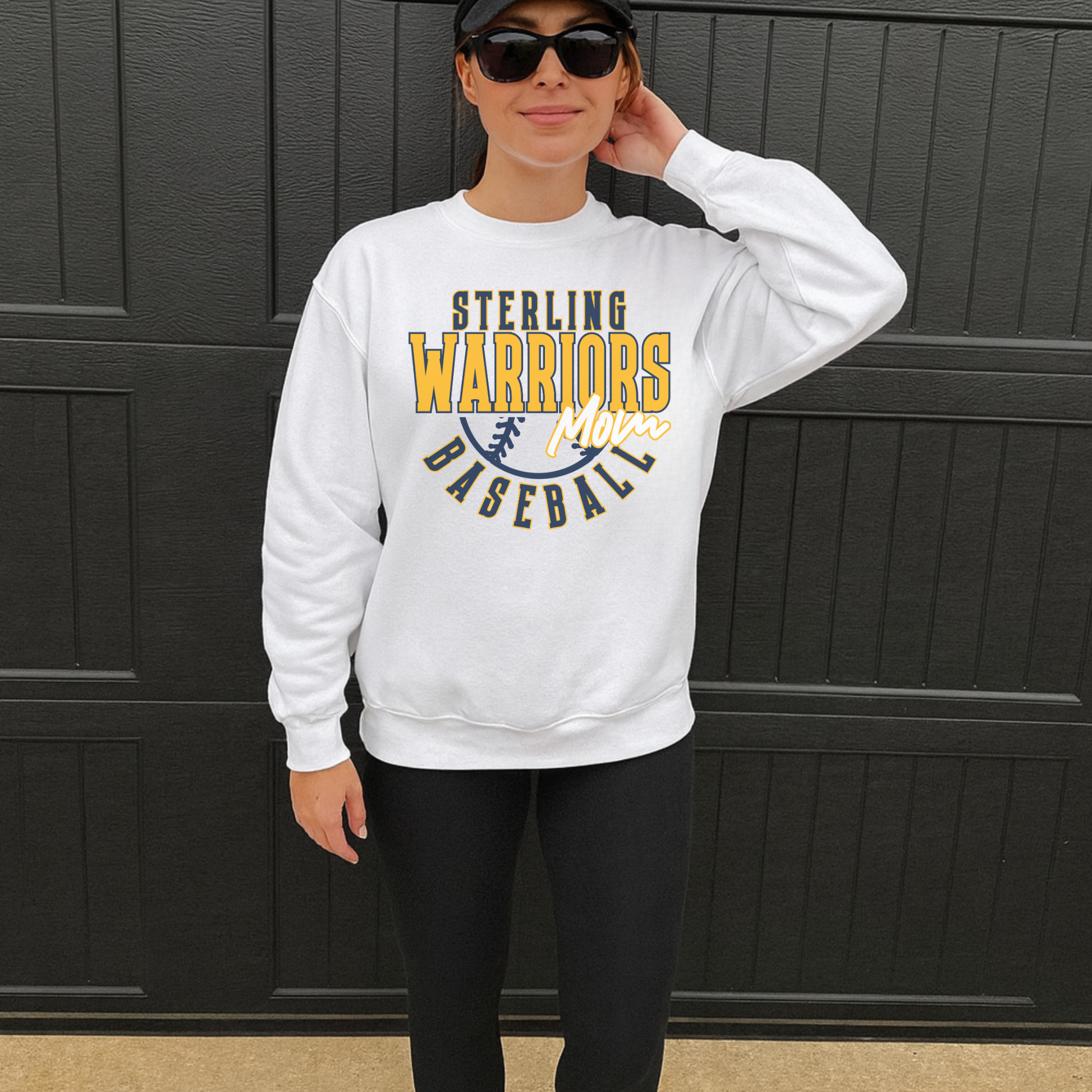 Sterling Warriors Baseball Mom white crewneck sweatshirt worn by woman with black leggings and hat standing outdoors sporty casual outfit