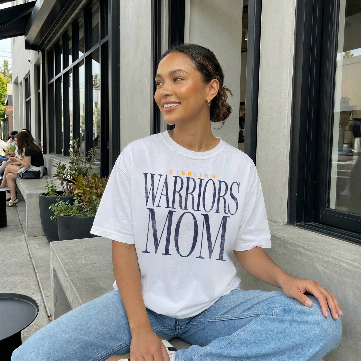 Sterling Warriors Mom white t-shirt worn by woman sitting outside cafe with jeans minimalist sporty mom outfit