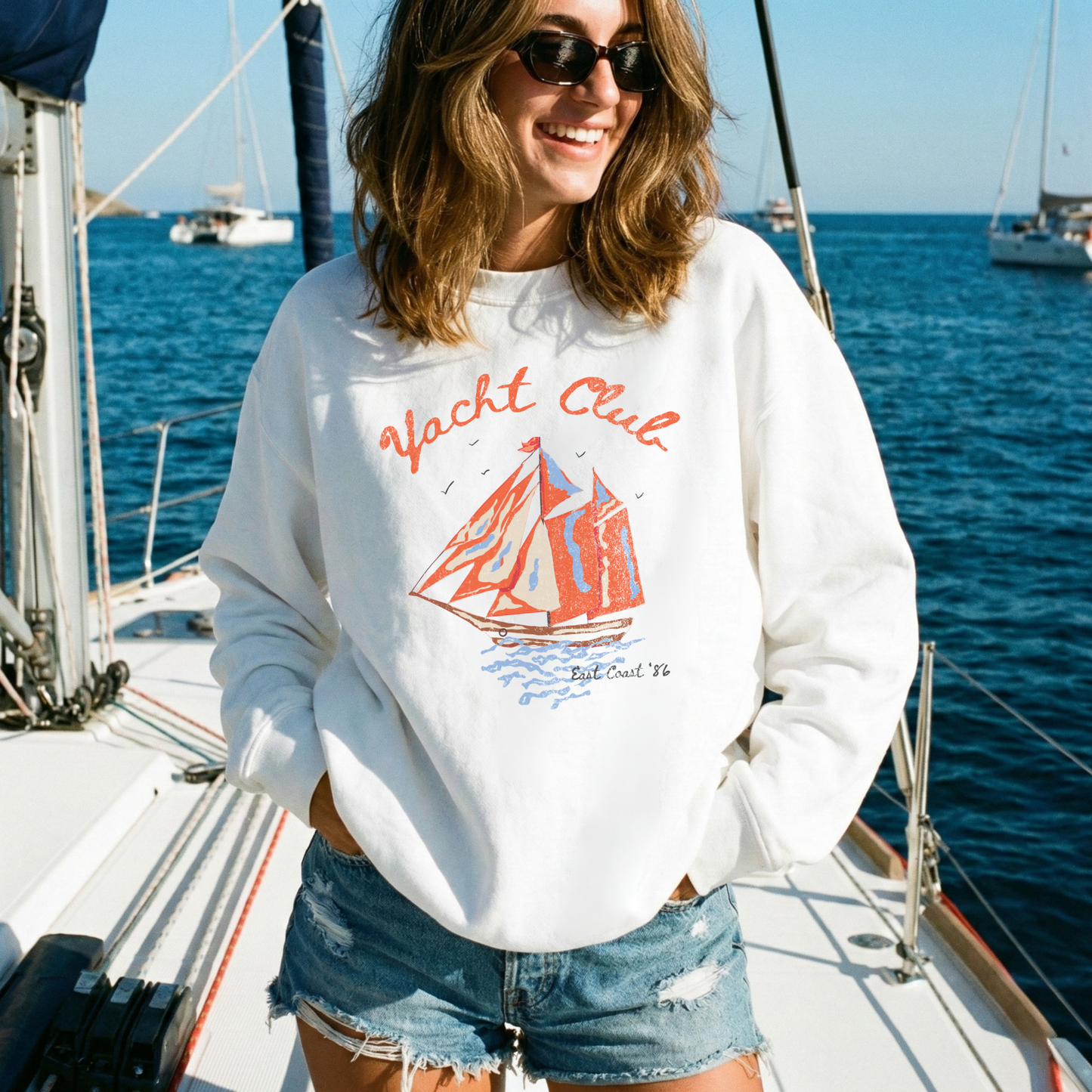woman wearing oversized white yacht club sweatshirt on sailboat coastal vacation outfit
