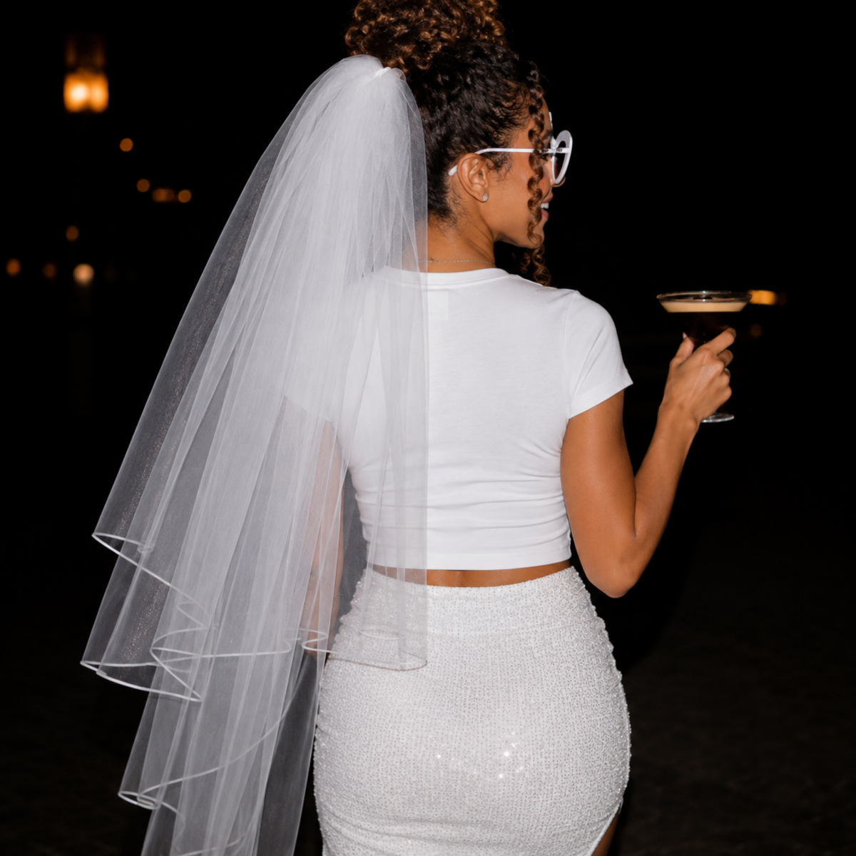 Bride-to-be wearing white fitted baby tee with veil and white sequin skirt