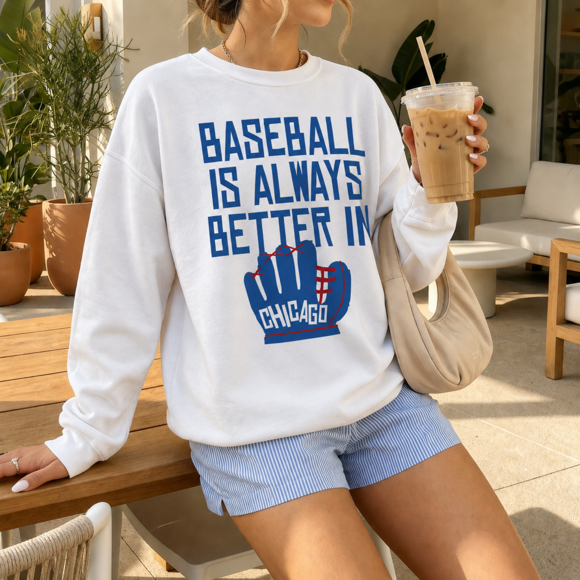 Woman wearing oversized white Baseball Is Always Better In Chicago sweatshirt with blue and red baseball glove graphic holding iced coffee