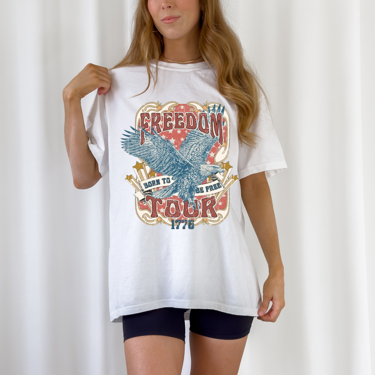 A person wearing a white graphic tee with 'Freedom Tour 1776' text and an eagle design.