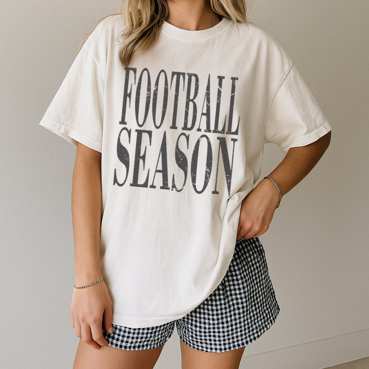 Person wearing a white 'Football Season' t-shirt and checkered shorts on a neutral background
