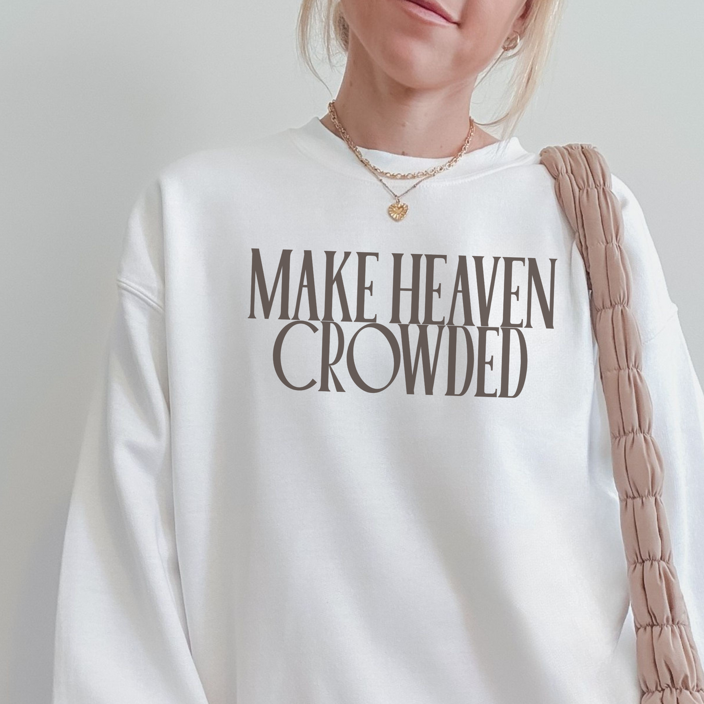 Person wearing a white sweatshirt with 'MAKE HEAVEN CROWDED' text on a plain background
