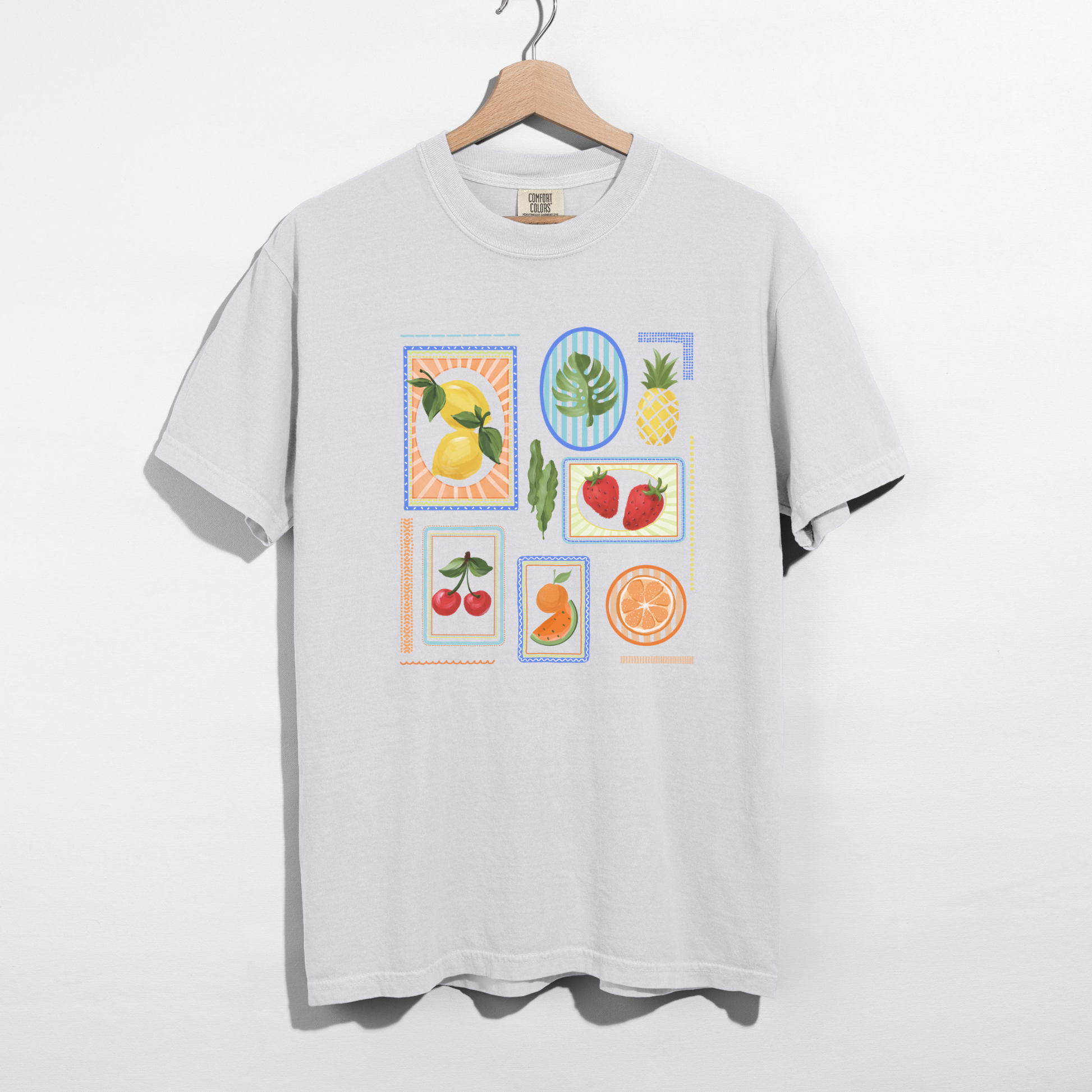 White fruit block graphic tee hanging on wooden hanger against white background.