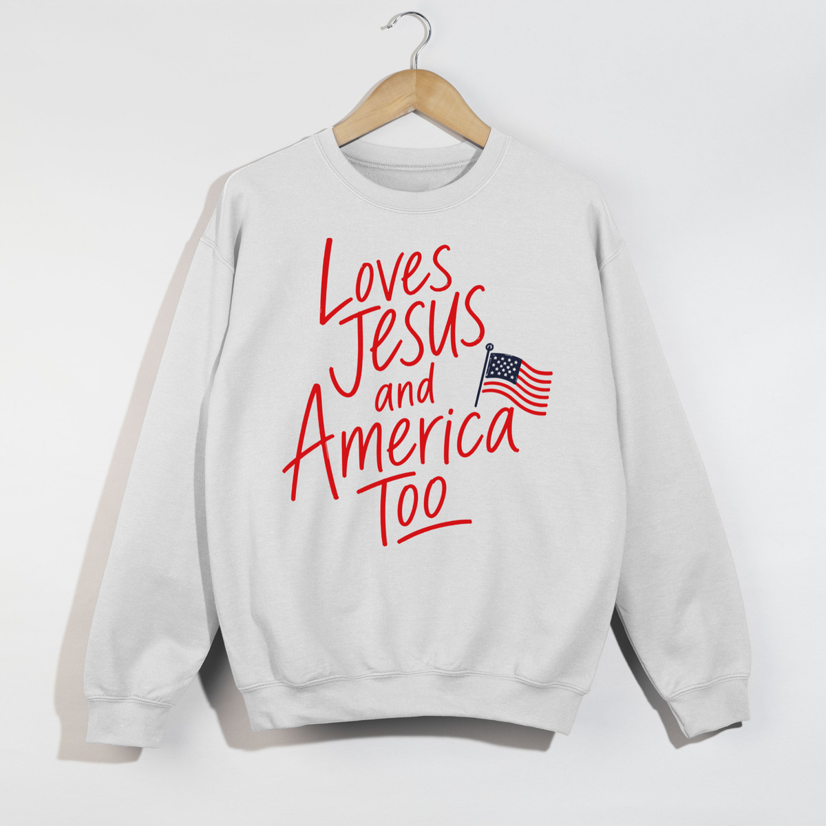 Loves Jesus and America Too patriotic Christian sweatshirt with red script lettering and American flag graphic on white crewneck sweatshirt