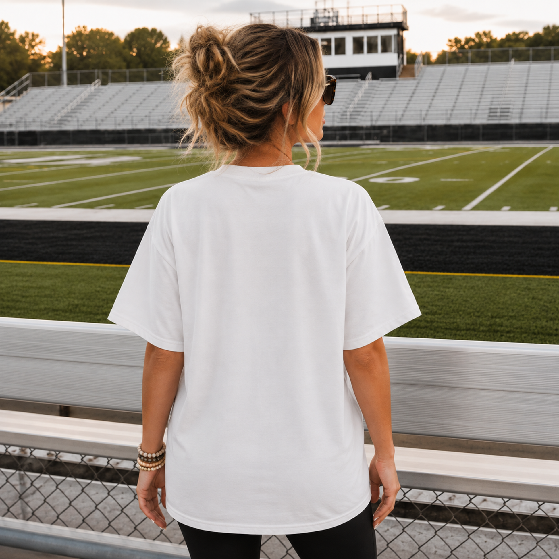Back view of woman wearing white football game day graphic tee at stadium bleachers