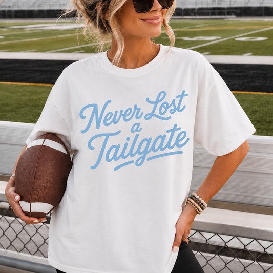 Woman wearing Never Lost a Tailgate white graphic tee with baby blue lettering at football stadium