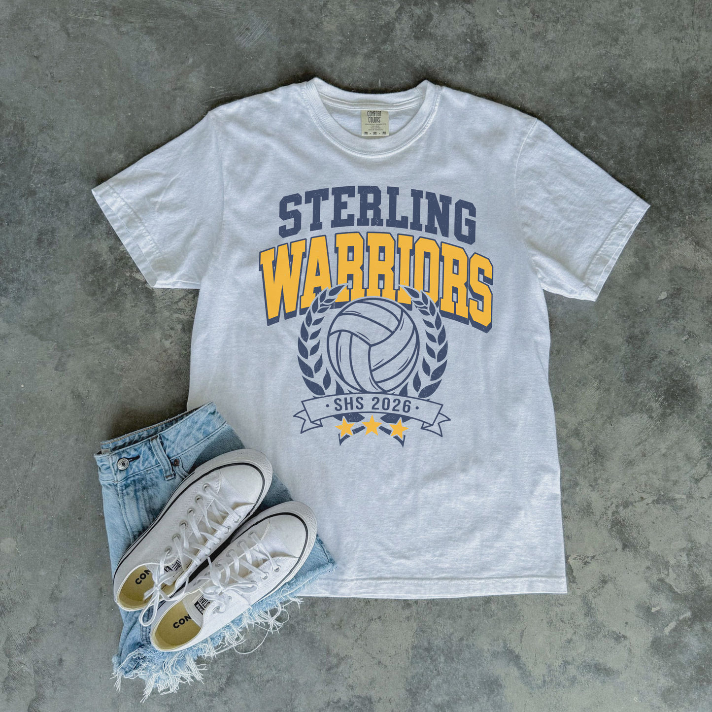 White Sterling Warriors Volleyball Comfort Colors graphic t-shirt flat lay with denim shorts and white sneakers featuring varsity volleyball design.