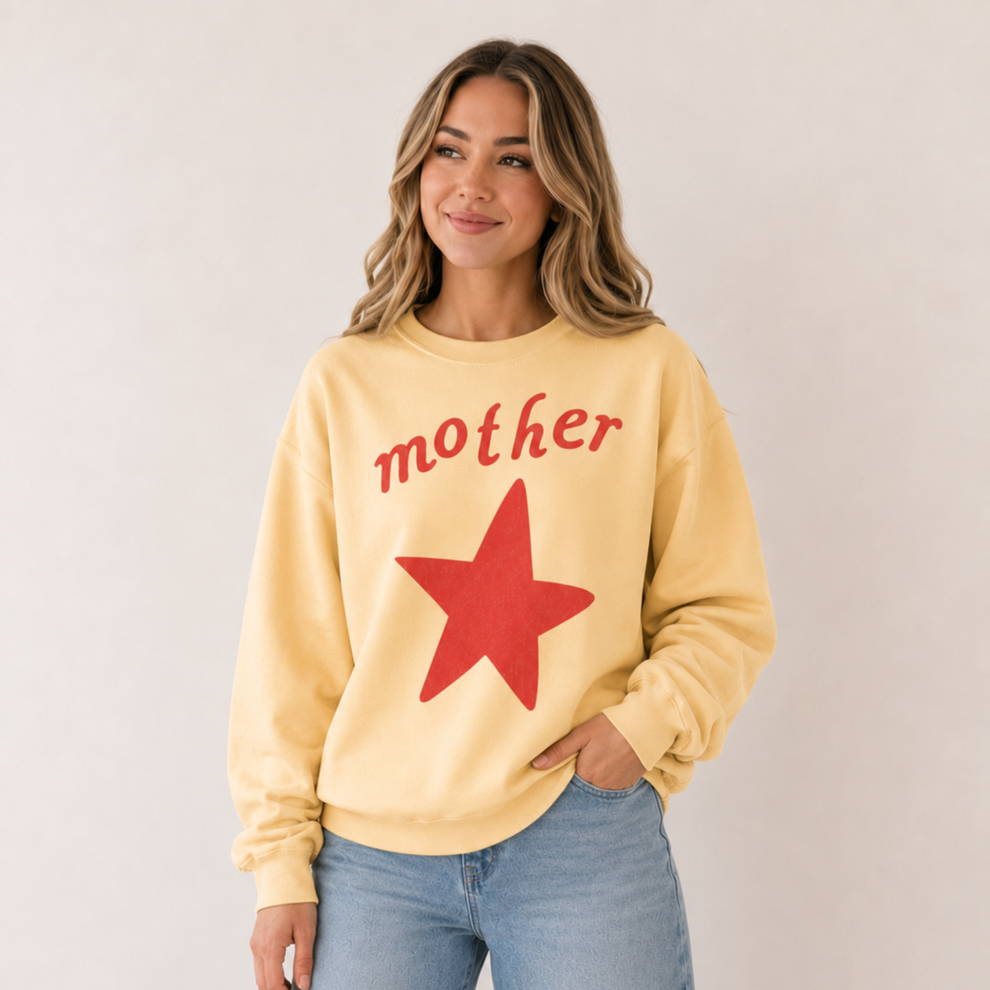 Mother wearing a butter yellow graphic sweatshirt with red vintage mother lettering and oversized star design paired with light wash denim jeans.
